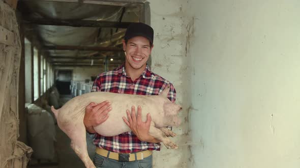 A Farmer Holds a Pig From the Farm in His Arms