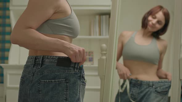 30s Woman Measuring Her Waistline with Measuring Tape Looking at the Mirror