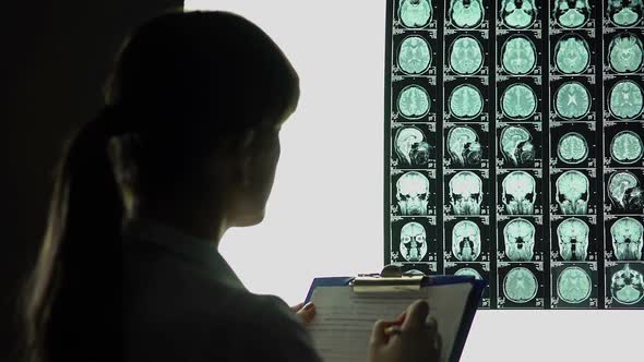 Female Neurologist Looking Thoughtfully at Brain X-Ray, Writing Down Diagnosis