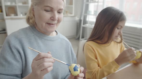 Cheerful Senior Woman and Granddaughter Decorating Easter Eggs