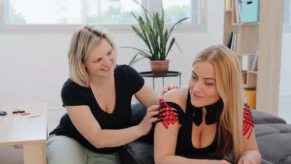 Physical therapist applying kinesio tape on female patient's shoulder.