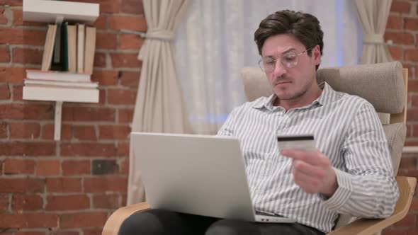 Middle Aged Man making Online Payment on Laptop on Sofa