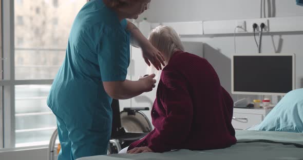 Nurse Brushing Gray Hair of Elderly Woman Patient in Hospital Ward