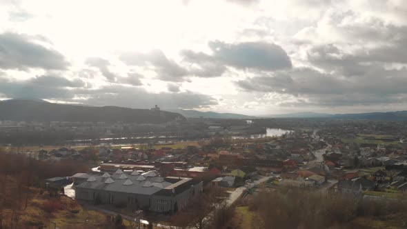 Forward Aerial Drone over outskirts of small city with silhouette castle on hill in background