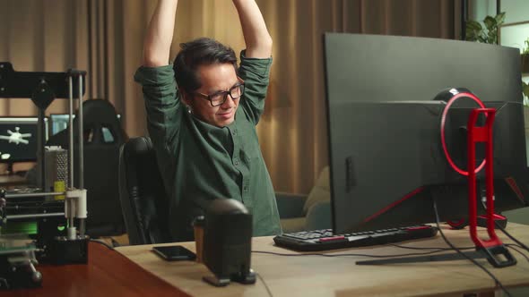 Asian Man Stretching While Works On Personal Computer And 3D Printer In Home Office