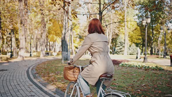 Back View of Unknown Redhead Female Riding Her Cruiser Bike By Tiled Path of City Park