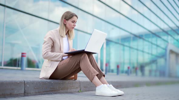 young business woman sitting on the sidewalk and working on laptop 