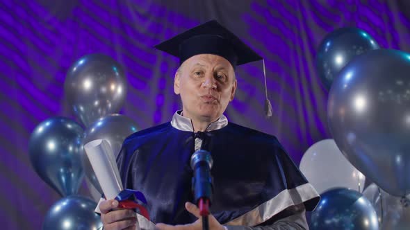 Male Teacher in Academic Dress Congratulates Students on Graduation Speaks Into Microphone While