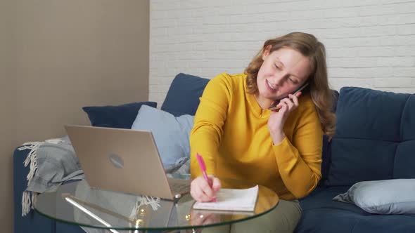 Woman Works at Laptop at Home and is in Hurry Writes Something and Talks on the Phone