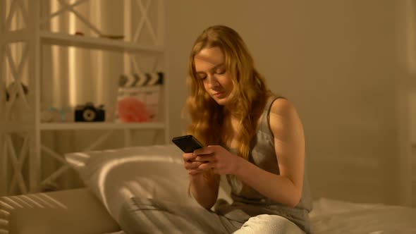 Smiling Female Student Typing Message by Smartphone Application Sitting Home Bed