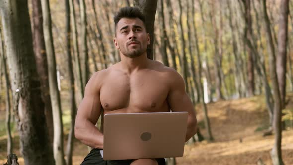 Strong Naked Torso Guy Sits In An Autumn Park With Laptop In His Hands.