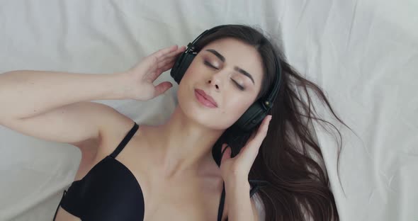 Girl Listening to Music on Bed Looks Into Camera and Twists Headphones' Wire