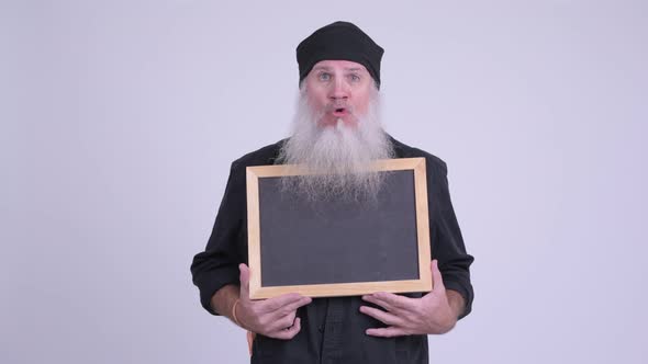 Mature Bearded Hipster Man Looking Shocked While Holding Blackboard