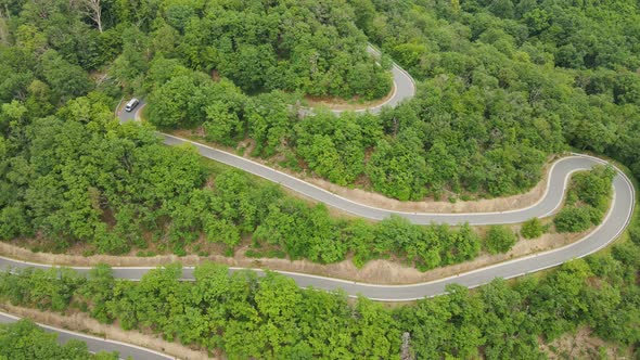 Large RV driving down a narrow, winding mountain road with several switchbacks on a sunny summer day