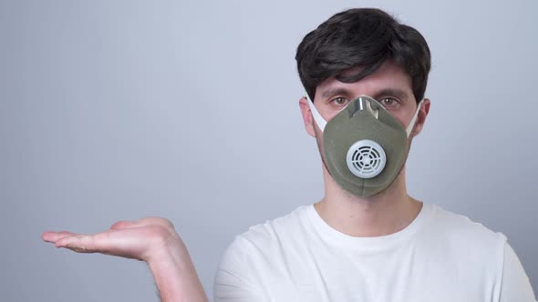 Man in a Respirator Showing and Presenting with Open Hand Palm on a Gray Background.