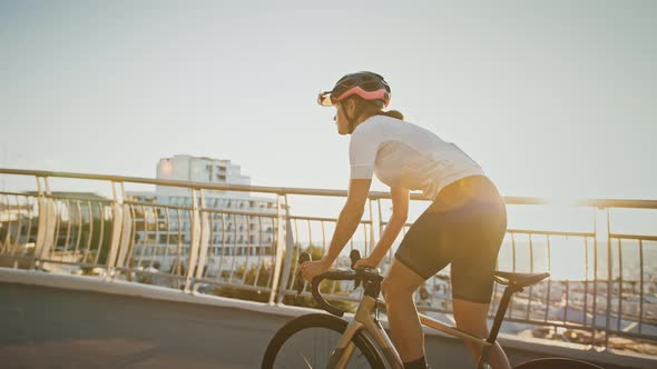 Girl in Sportswear and Protective Helmet is Riding Sports Bike Uphill Along Bridge Surrounded By