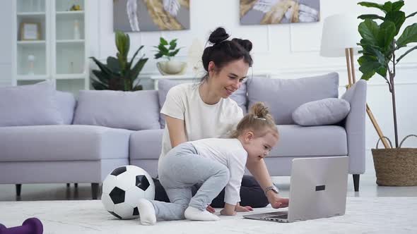 Young Brunette Sitting on the Carpet with Her Playful Funny Daughter and Trying to do Yoga