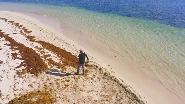 Man works cleaning seaweed at Punta Cana beach, Dominican Republic. Aerial drone circling pov