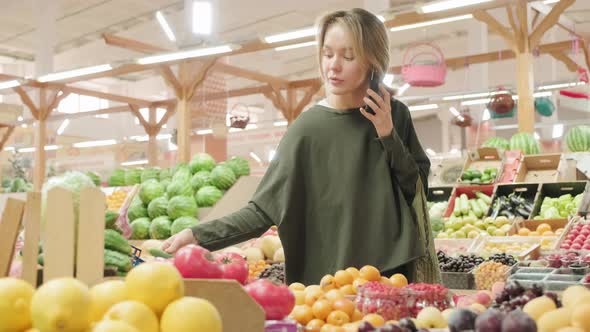 Woman Talking on Phone and Choosing Fresh Vegetables at Market