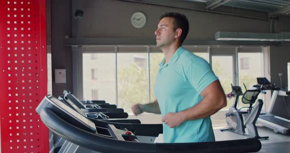 Side View at Young Man Running on Treadmill at Gym, Slow Motion