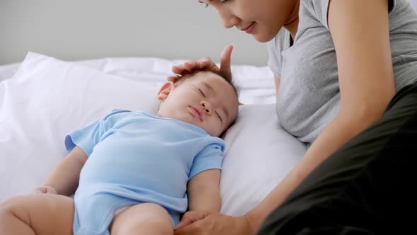 Sleeping little baby with young mother on bed.