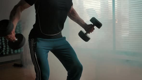 Muscled Sporty Man Working on Biceps with Huge Layout Heavy Dumbbells in Gym