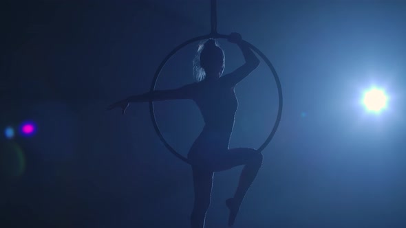 Silhouette of Flexible Aerial Gymnast Rotates on an Aerial Ring and Performs Acrobatic Tricks in the