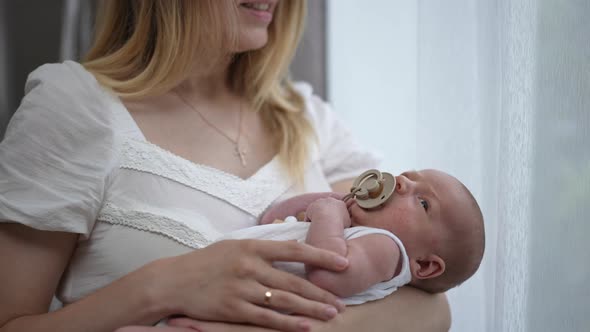 Calm Caucasian Newborn Boy Sucking Pacifier in Slow Motion Lying on Hands of Unrecognizable Woman