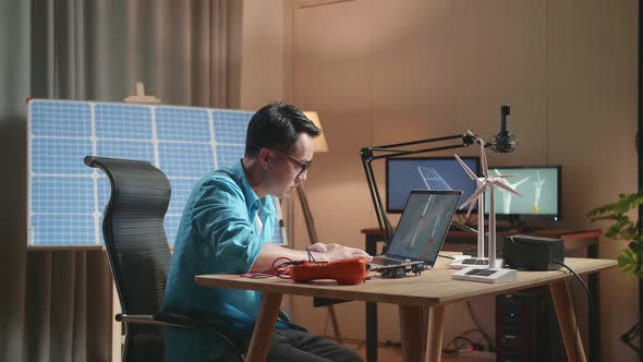 Asian Man Looking At A Laptop Showing Wind Turbine On The Table That Next To The Solar Cell