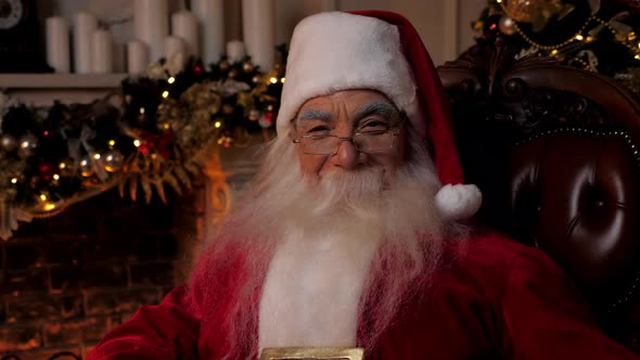 Close Up Smiling Santa Claus Looks Looks Camera Sitting on Chair at Home