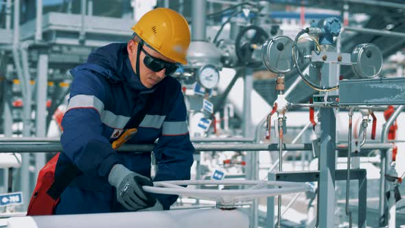 A modern worker in the oil industry rotates a valve for supplying fuel through an oil pipeline