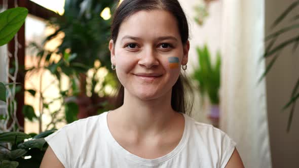 A Smiling Young Ukrainian Girl with the Flag of Ukraine on Her Face is Looking to Camera