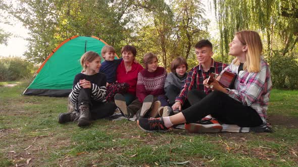 Group of Happy People with Children Sing While Relaxing on Summer Vacation on Camping Trip