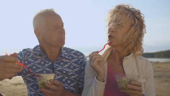 Elderly Wife and Husband Eating Tasty Salad Having Picnic on Sea Beach