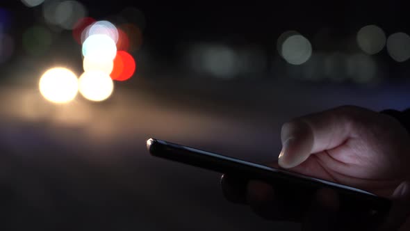 Hand With a Smartphone on the Background of Passing Cars Headlights