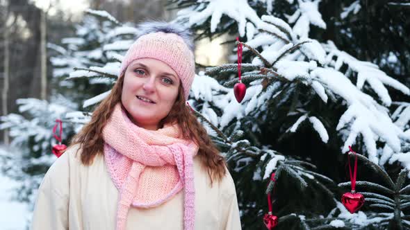 Happy woman looks at Christmas tree toy in winter forest