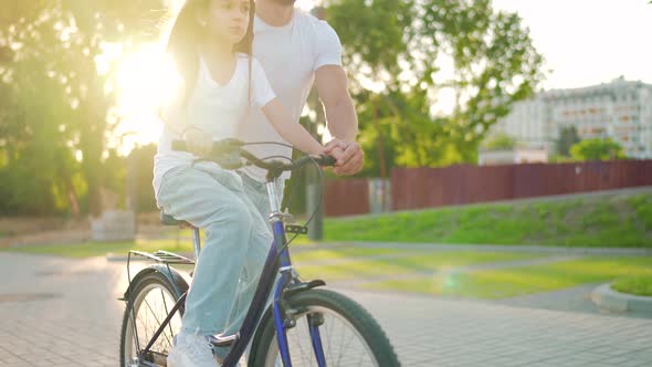 Dad is Teaching Daughter How to Ride Bicycle at Sunset