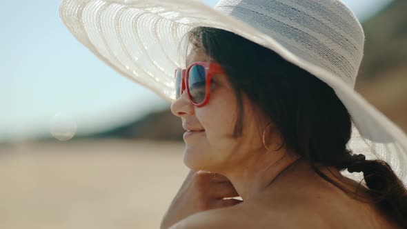 A Young Girl in a White Hat Sits on the Seashore and Looks Into the Distance