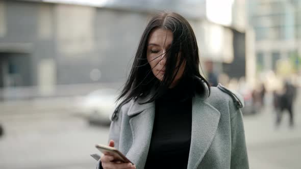 Portrait of Adult Townswoman in City Centre in Autumn Day Brunette Lady is Holding Cell Phone