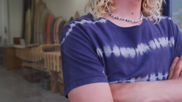 Caucasian male surfboard maker leaning on a door frame of the entrance with his arms crossed