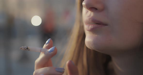 Closeup of a Beautiful Pensive Girl Who Smokes Outdoors on a Sunny Day