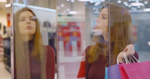 Young Woman Holding Bags with Purchase Staring at Shop Window