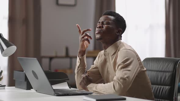 Black Man is Trying to Be Concentrated on Work Sitting at Table with Open Laptop and Thinking Hardly