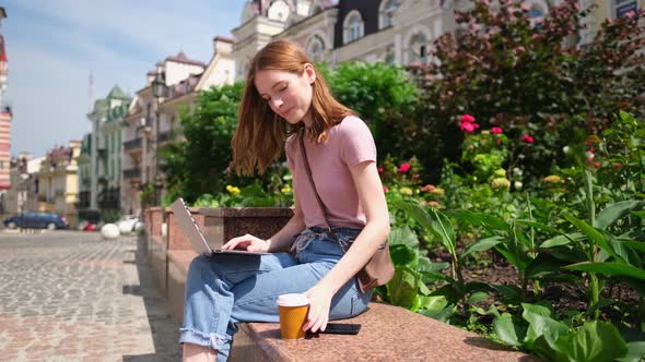 Beautiful Young Woman Tourist with Takeout Coffee in the City Center Using Laptop