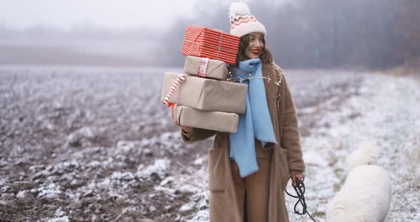 Woman with Dog Carrying Gift Boxes on the Snowy Field