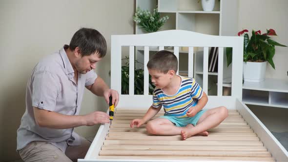Father and Son Together Assemble a Children's Bed Screw Screws with a Screwdriver