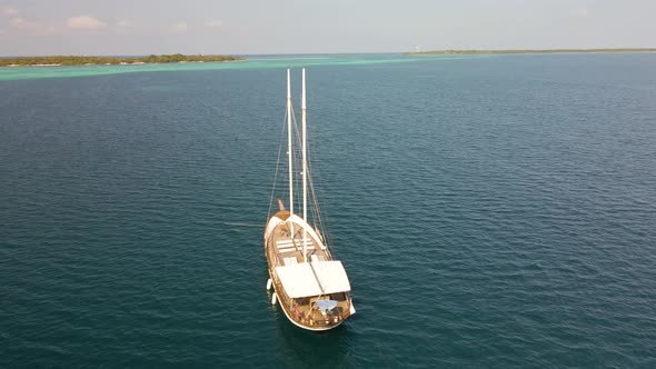 Pitchfork from above on a yacht sailing on blue water next to a maldivian island with green trees