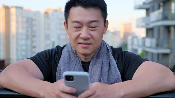 Asian Man with a Towel Around His Neck Holds a Mobile Phone Looking to Camera
