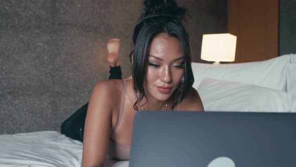 Woman Freelancer with Computer Lying on a Bed in Hotel Room