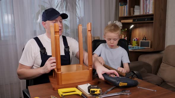 A Builder Father in Overalls Teaches His Son How to Repair a Wooden Chair